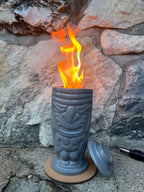 Rencarie Tiki tabletop fire pit lit with a tall flame against a stone wall