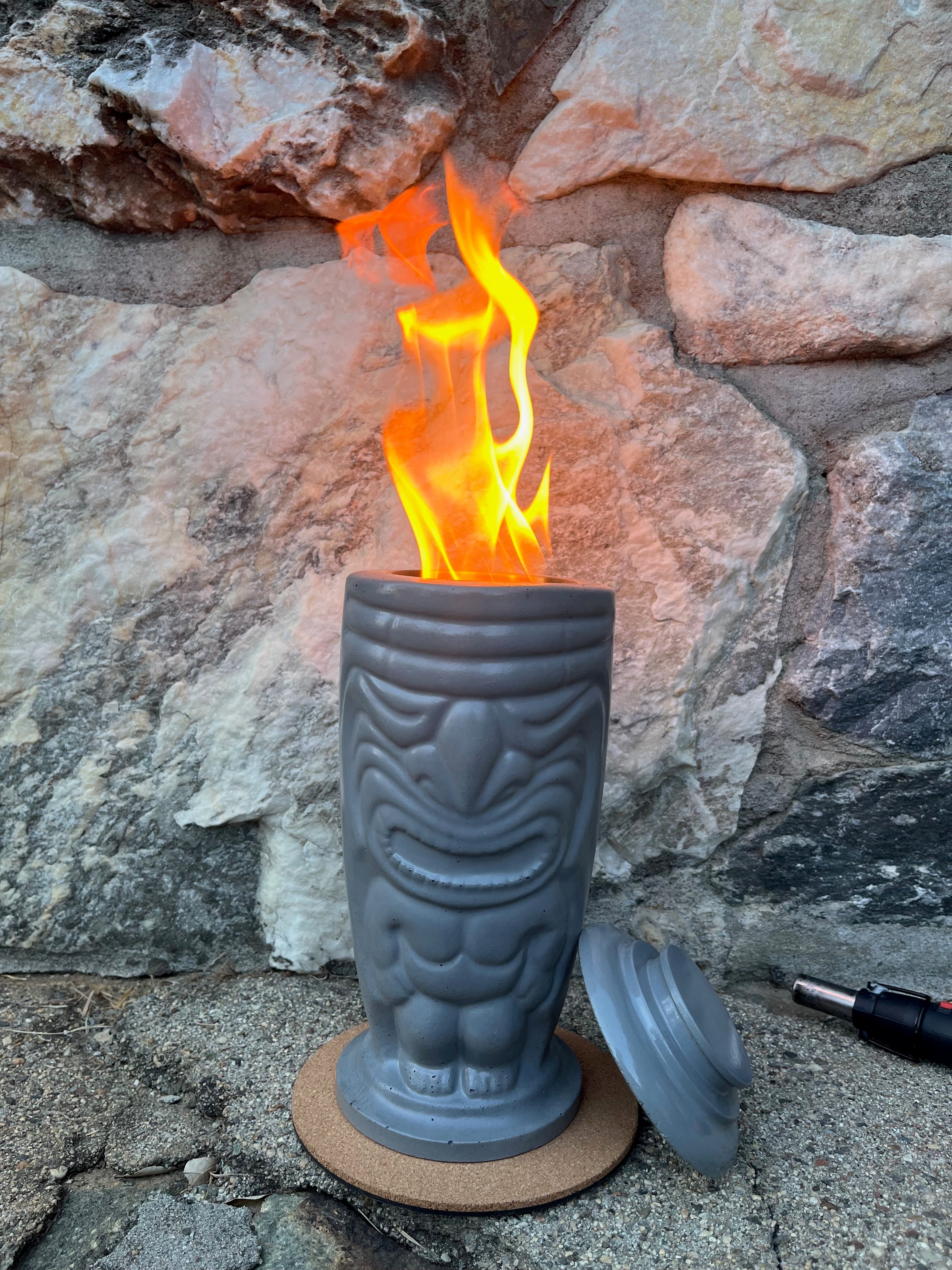 Rencarie Tiki tabletop fire pit lit with a tall flame against a stone wall