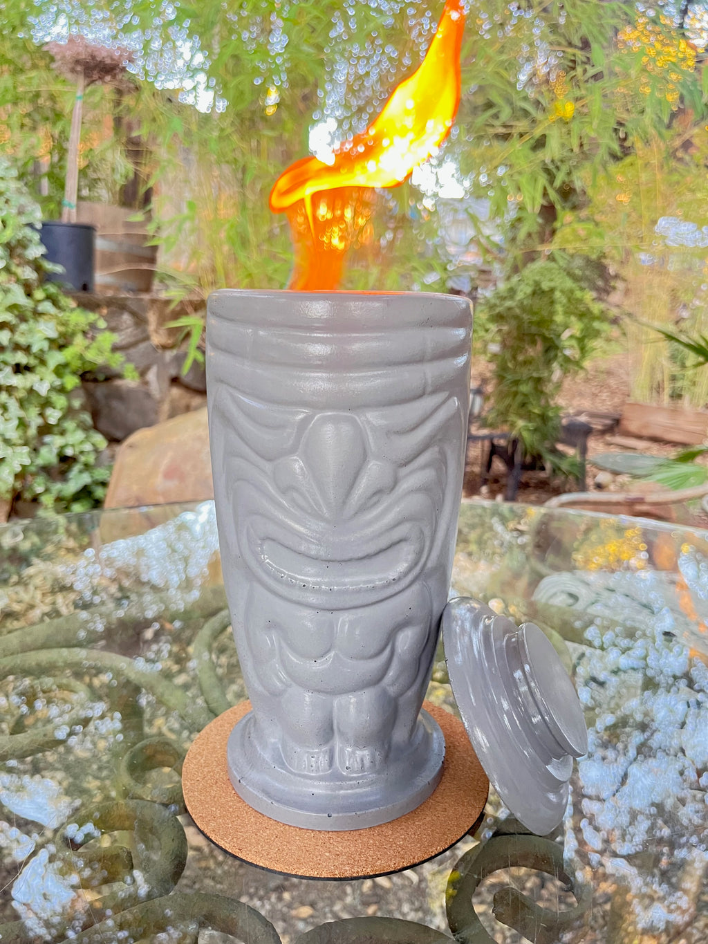 Rencarie Tiki tabletop fire pit in light grey, lit, on a glass patio table